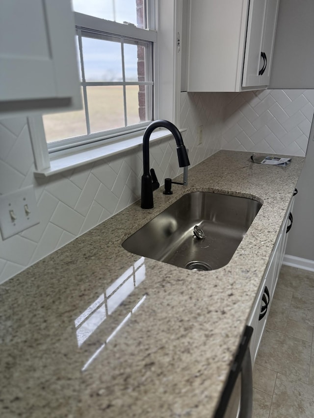 kitchen featuring white cabinetry, light stone counters, a sink, and tasteful backsplash