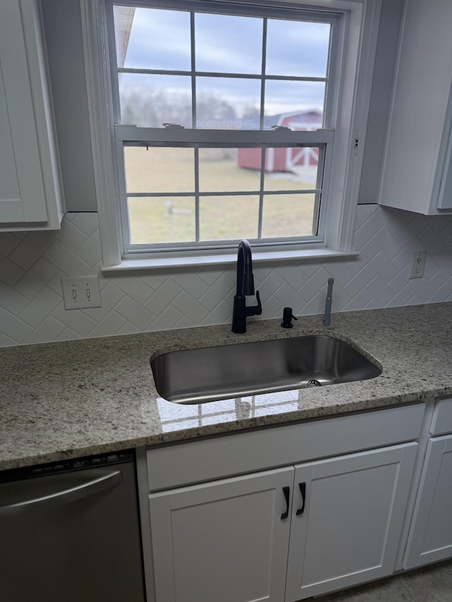kitchen featuring decorative backsplash, light stone countertops, white cabinets, a sink, and dishwasher