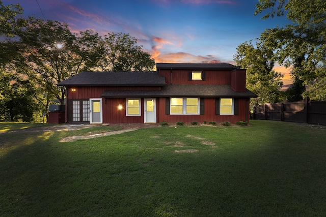 back house at dusk featuring a lawn