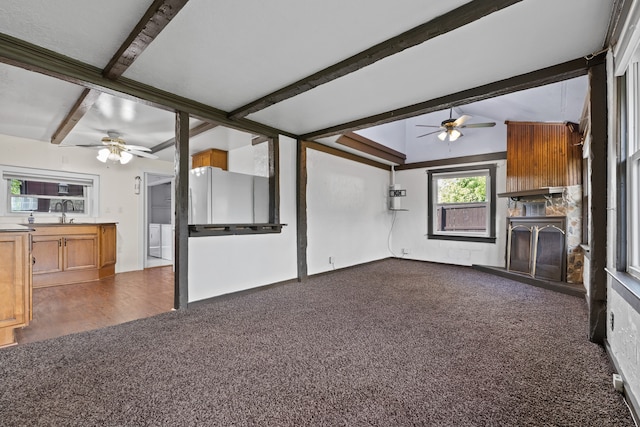 unfurnished living room featuring ceiling fan, sink, dark colored carpet, and vaulted ceiling with beams