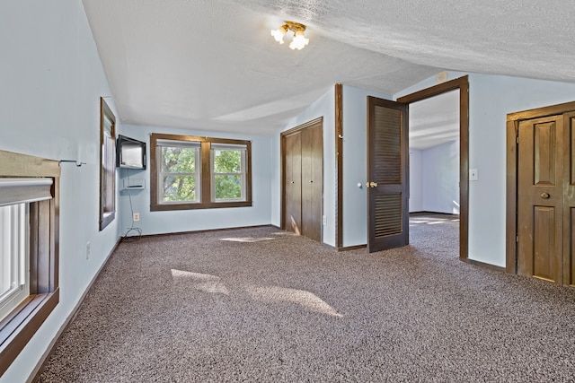 unfurnished bedroom with vaulted ceiling, a textured ceiling, and carpet