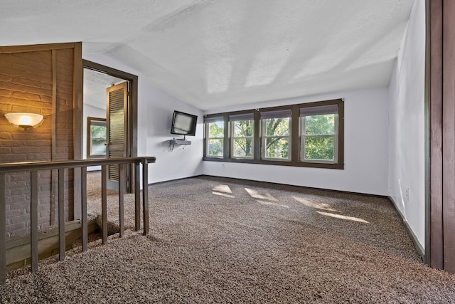 carpeted empty room featuring vaulted ceiling and a textured ceiling