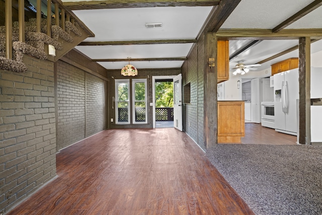 unfurnished living room featuring dark wood-type flooring, brick wall, beam ceiling, and ceiling fan