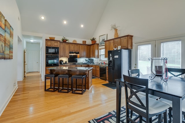 kitchen featuring a kitchen island, black appliances, a kitchen bar, high vaulted ceiling, and light wood-type flooring