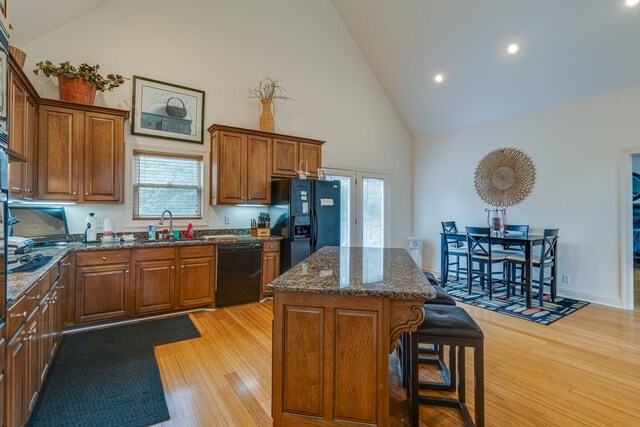 kitchen with light hardwood / wood-style flooring, black appliances, a center island, high vaulted ceiling, and dark stone counters