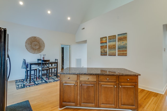 kitchen featuring dark stone counters, lofted ceiling, stainless steel refrigerator, and light hardwood / wood-style floors