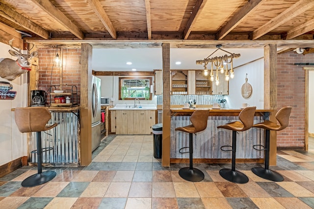 kitchen with brick wall, pendant lighting, light brown cabinetry, appliances with stainless steel finishes, and sink