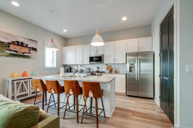 kitchen featuring pendant lighting, light hardwood / wood-style flooring, stainless steel appliances, and white cabinets