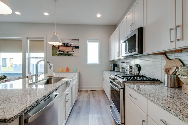 kitchen with pendant lighting, light hardwood / wood-style flooring, sink, appliances with stainless steel finishes, and white cabinets