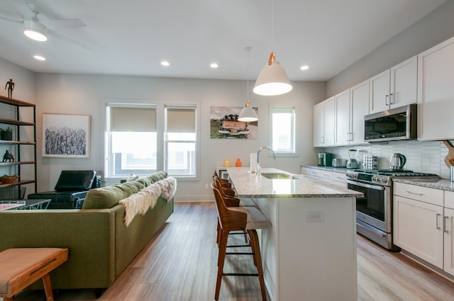 kitchen with pendant lighting, white cabinetry, sink, appliances with stainless steel finishes, and light hardwood / wood-style floors