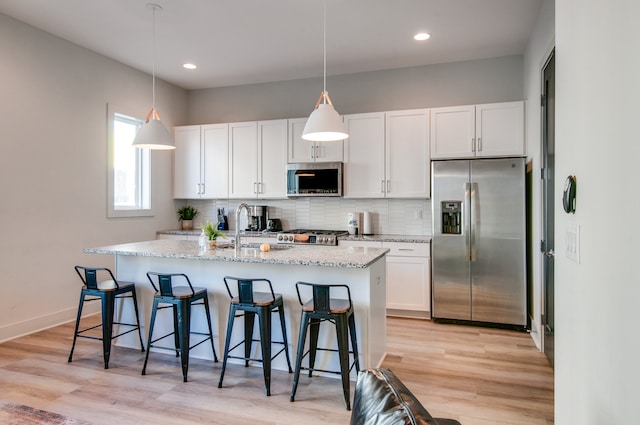 kitchen with white cabinets, stainless steel appliances, light hardwood / wood-style floors, sink, and an island with sink