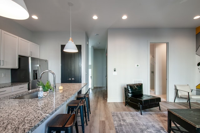 kitchen featuring light hardwood / wood-style flooring, stainless steel fridge with ice dispenser, sink, white cabinetry, and light stone counters