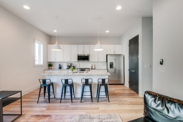 kitchen featuring hanging light fixtures, stainless steel appliances, white cabinetry, and a kitchen island with sink