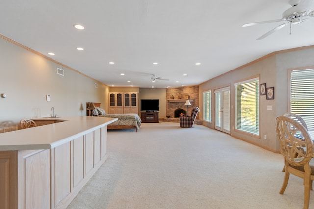 carpeted bedroom with a large fireplace, access to exterior, ornamental molding, sink, and ceiling fan