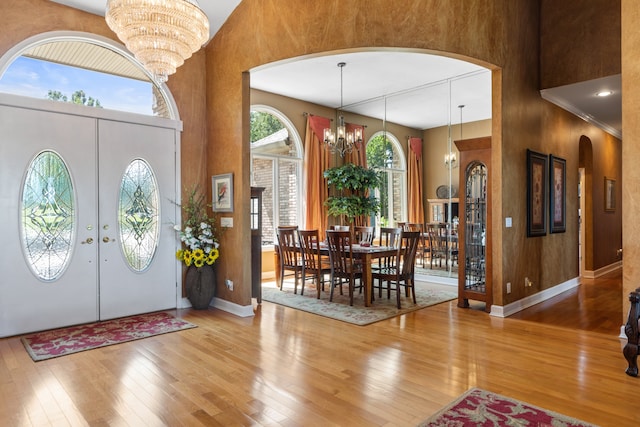 entryway featuring french doors, an inviting chandelier, light hardwood / wood-style floors, and a towering ceiling