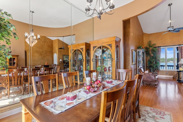 dining room with ceiling fan with notable chandelier, high vaulted ceiling, and hardwood / wood-style floors