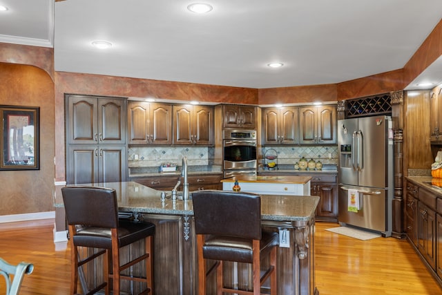 kitchen featuring a breakfast bar area, tasteful backsplash, a kitchen island with sink, stainless steel appliances, and light wood-type flooring