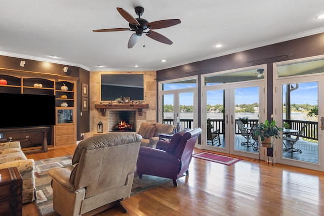 living room with light wood-type flooring, ornamental molding, a brick fireplace, ceiling fan, and french doors