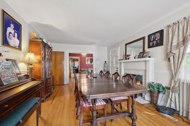 dining space with light wood-type flooring, ornamental molding, and a brick fireplace