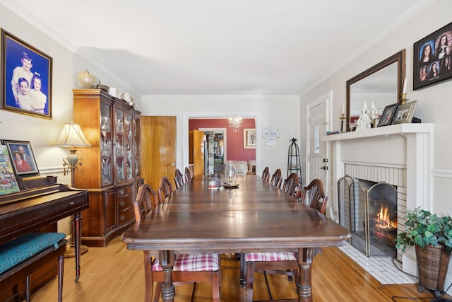 dining space with light hardwood / wood-style flooring, an inviting chandelier, crown molding, and a brick fireplace