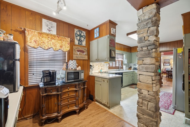 kitchen with wooden walls, light tile patterned floors, stainless steel appliances, green cabinetry, and ornate columns