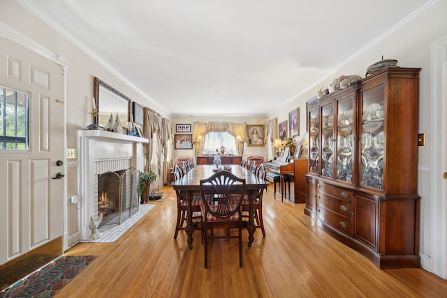 dining room featuring light hardwood / wood-style flooring, ornamental molding, and a brick fireplace