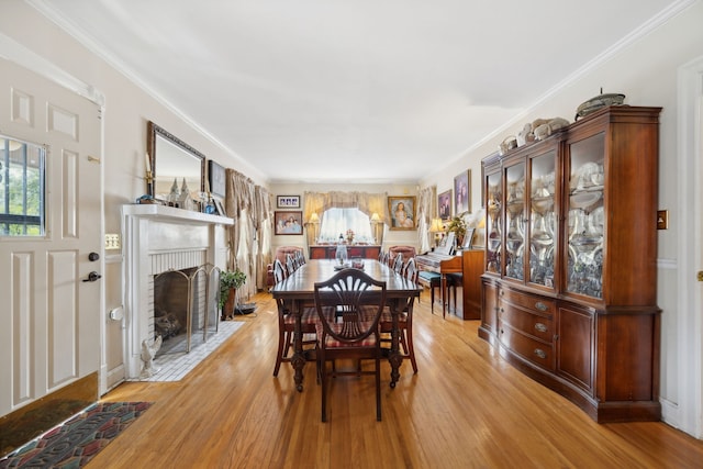 dining space featuring a fireplace, light wood-type flooring, and ornamental molding