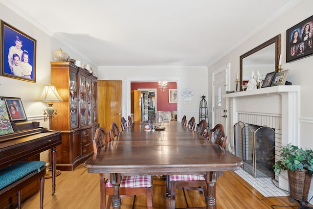 dining space featuring crown molding, light hardwood / wood-style floors, a notable chandelier, and a fireplace