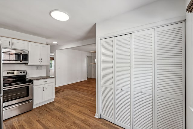 kitchen with wood-type flooring, dark stone countertops, stainless steel appliances, and white cabinetry