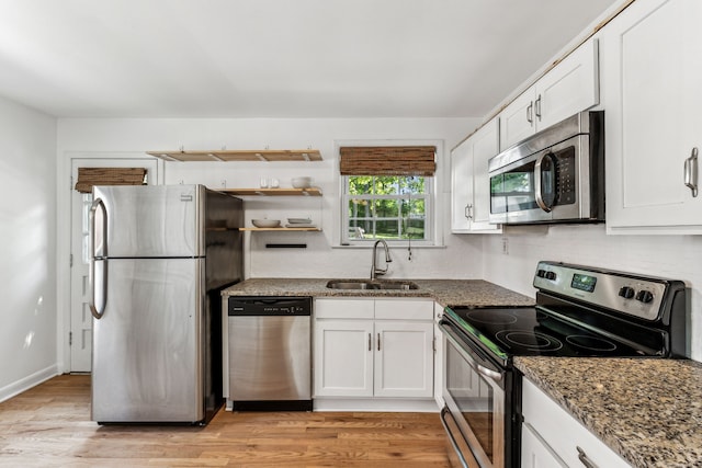 kitchen featuring white cabinets, dark stone countertops, appliances with stainless steel finishes, light hardwood / wood-style floors, and sink