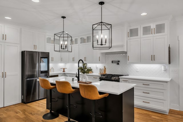 kitchen featuring a notable chandelier, stainless steel fridge, light hardwood / wood-style flooring, an island with sink, and white cabinets