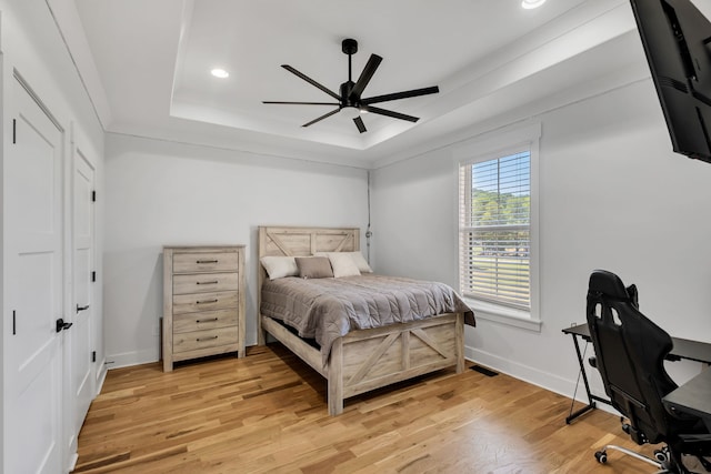 bedroom with light wood-type flooring, a tray ceiling, and ceiling fan