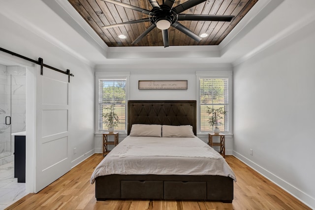 bedroom featuring ensuite bath, ceiling fan, a tray ceiling, a barn door, and light hardwood / wood-style floors