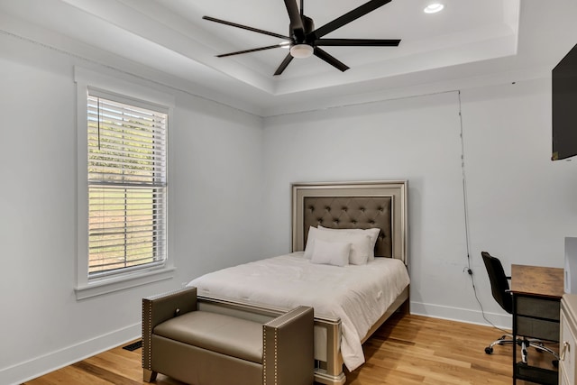 bedroom featuring ceiling fan, a raised ceiling, and light hardwood / wood-style floors