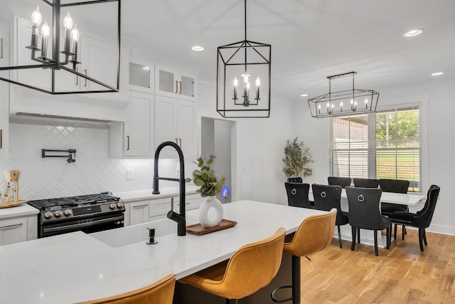 kitchen featuring light wood-type flooring, pendant lighting, stainless steel range, and white cabinets