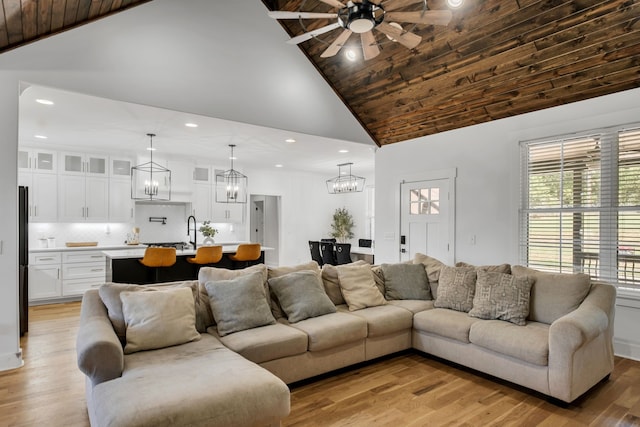 living room featuring light wood-type flooring, high vaulted ceiling, ceiling fan with notable chandelier, sink, and wood ceiling