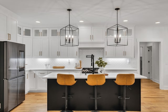 kitchen featuring white cabinets, an island with sink, stainless steel refrigerator, and a notable chandelier