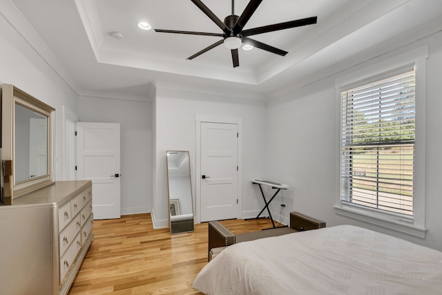 bedroom with light hardwood / wood-style flooring, ceiling fan, ornamental molding, and a tray ceiling