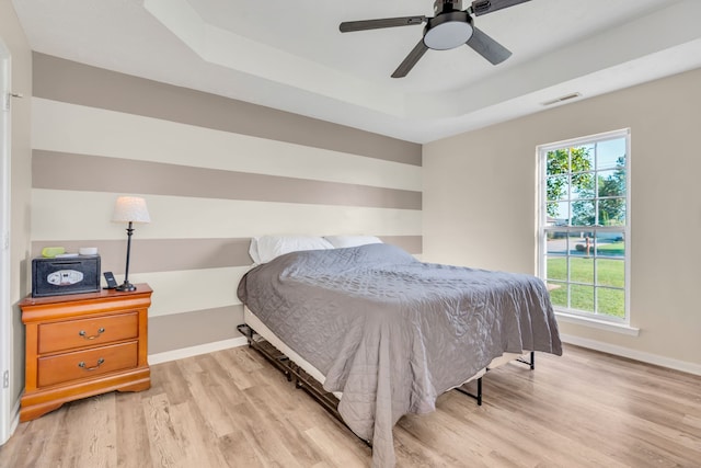 bedroom with a raised ceiling, ceiling fan, and light hardwood / wood-style floors