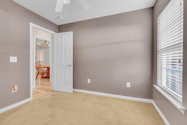 spare room with ceiling fan with notable chandelier and light colored carpet