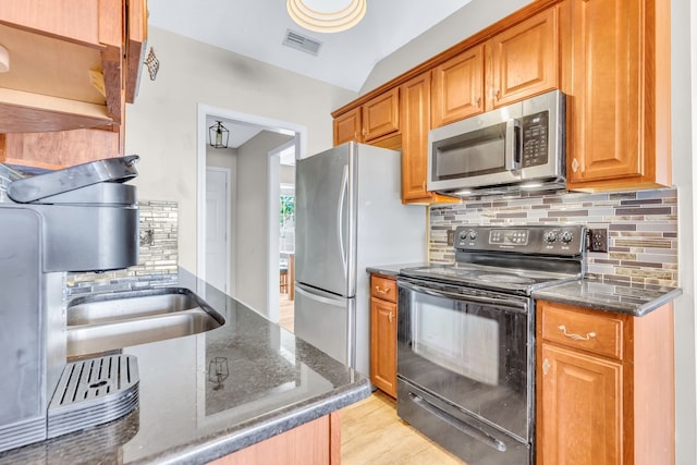 kitchen with dark stone countertops, tasteful backsplash, appliances with stainless steel finishes, lofted ceiling, and light hardwood / wood-style floors