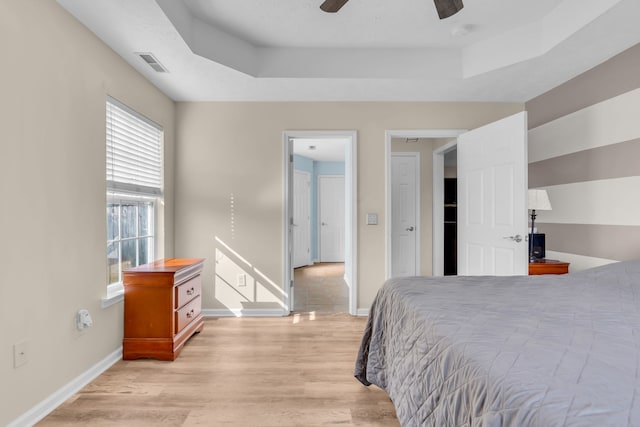 bedroom featuring a raised ceiling, ceiling fan, and light wood-type flooring