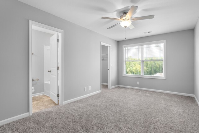 unfurnished bedroom with a spacious closet, a closet, ensuite bathroom, light colored carpet, and ceiling fan