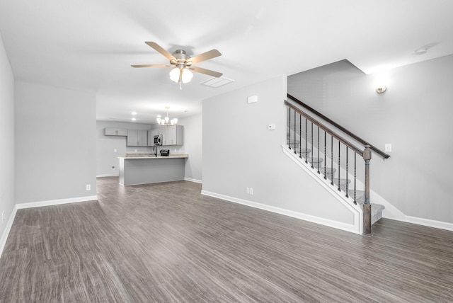 unfurnished living room featuring visible vents, baseboards, stairway, ceiling fan with notable chandelier, and dark wood-style floors