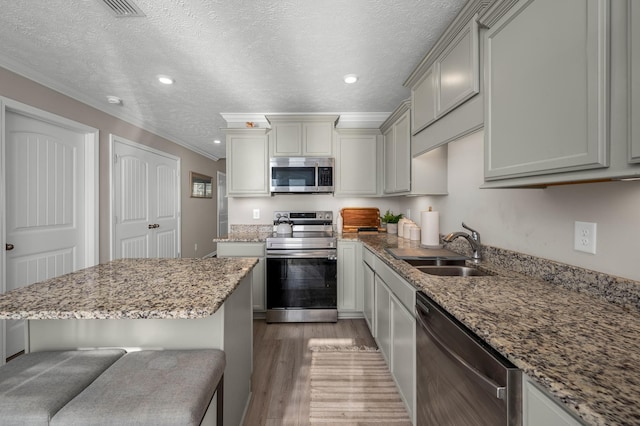 kitchen with a textured ceiling, a kitchen bar, stainless steel appliances, wood-type flooring, and sink