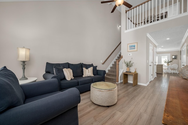 living room featuring light wood-type flooring, ceiling fan, crown molding, and a high ceiling