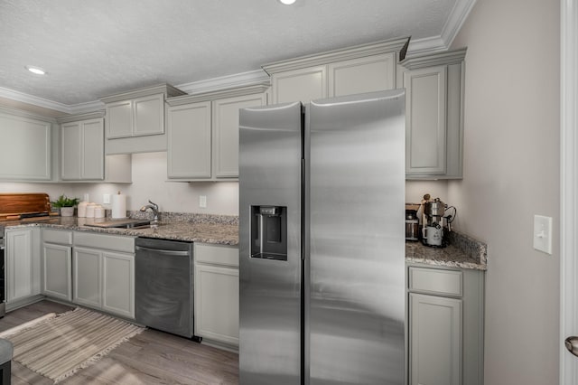 kitchen with crown molding, stainless steel appliances, light stone countertops, and light wood-type flooring