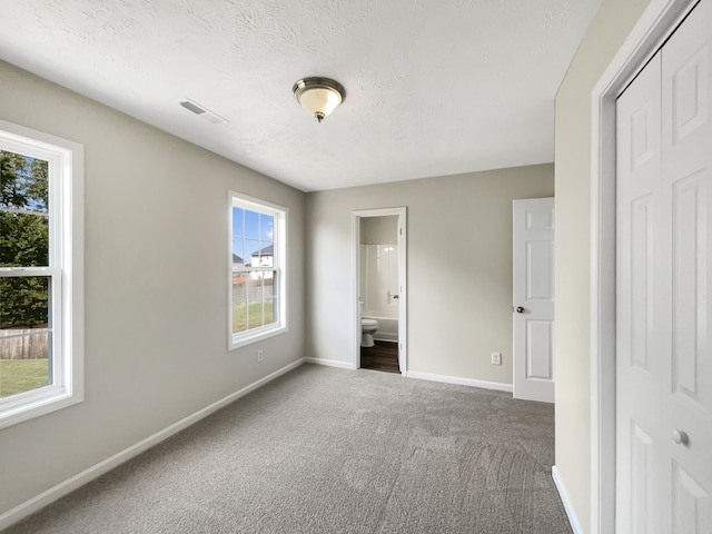 unfurnished bedroom with a closet, a textured ceiling, ensuite bathroom, and carpet