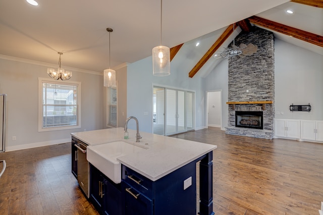 kitchen featuring ceiling fan with notable chandelier, a stone fireplace, beam ceiling, a center island with sink, and dark hardwood / wood-style floors