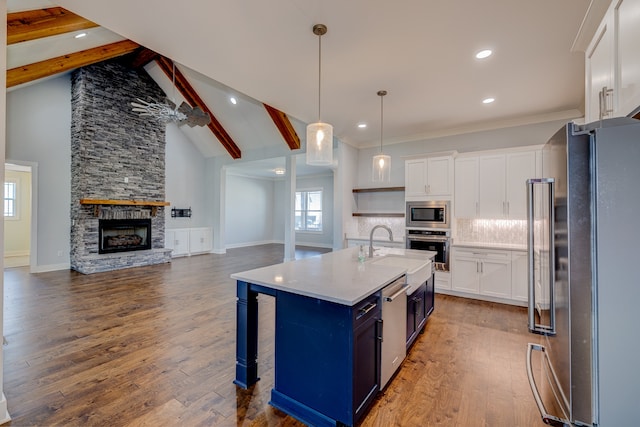 kitchen with white cabinets, stainless steel appliances, beam ceiling, ceiling fan, and a center island with sink